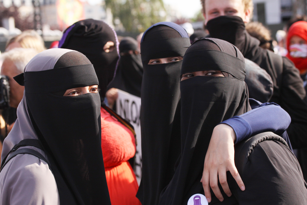 Four Muslim women in traditional full length niqab outdoors in a crowd.