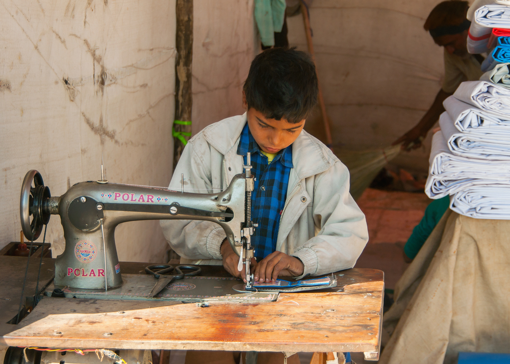 A child in India works at a sewing machine.