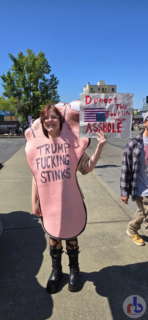 Woman in foot costume that says "Trump Fucking Stinks" holding sign "Deport this Foot into your Asshole"