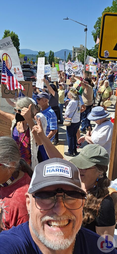"Radical" Russ selfie in "White Dudes for Harris" hat with hundreds of protestors behind him